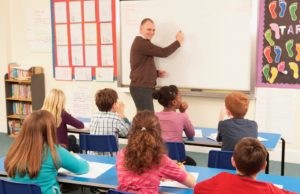 A man at the white board in a classroom full of children