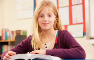 A young girl reads an open book in a classroom