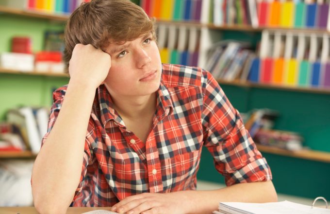 A young man thinking at a desk in a library