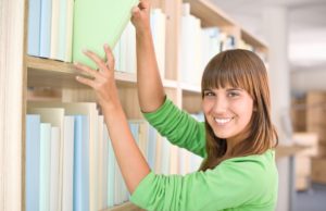 Woman looking happy in a library pulling a file of a shelf