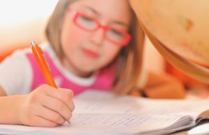 A young girl wearing glasses writes in a notebook