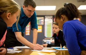 A male teacher helping students in a classroom