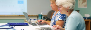 a gray-haired woman smiling in front of a laptop