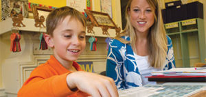 smiling teacher with student at a table with manipulatives