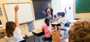 woman teacher in the front of classroom with students raising their hands