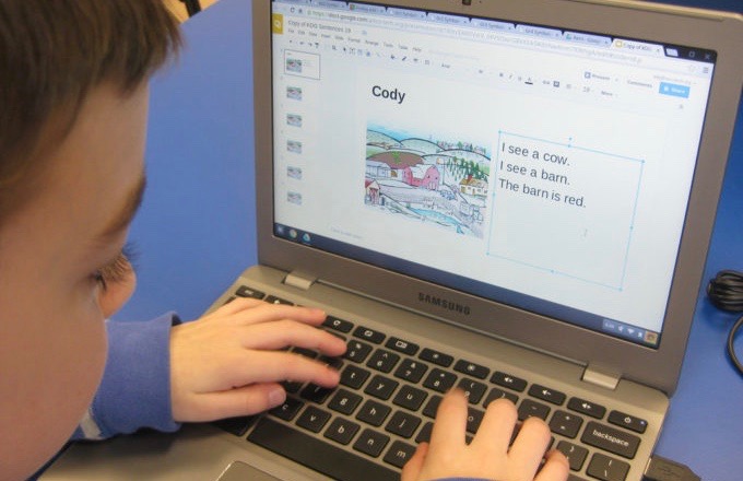 A young child types on a laptop at a blue desk