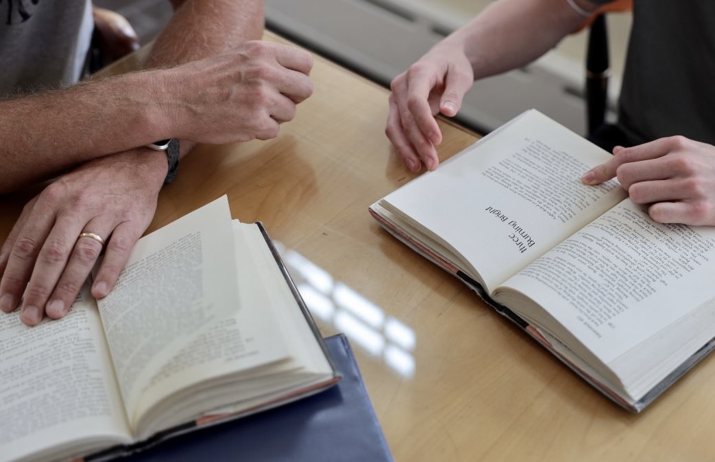 Two open novels with the hands of an educator and student.
