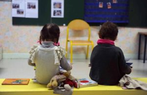 Two children sitting on a yellow bench in a classroom