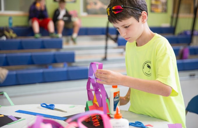 A young boy wearing a yellow tee-shirt completes a project