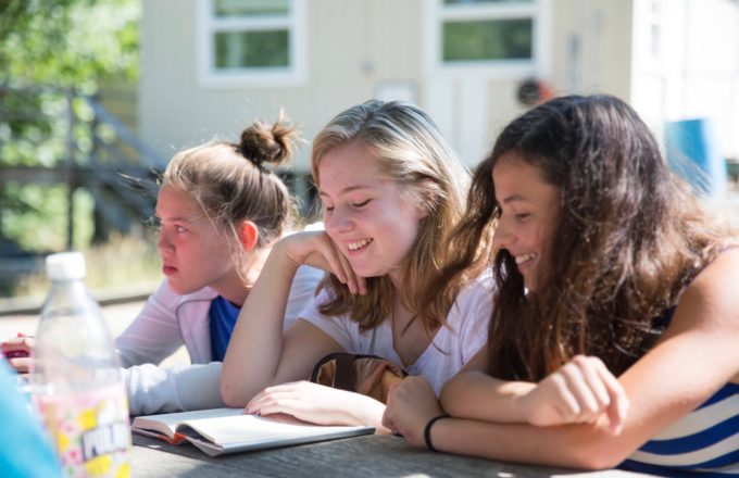 Three female students sitting outside reading a book