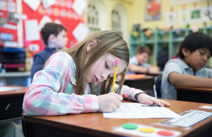 A young girl bends over a piece of paper writing with a pencil