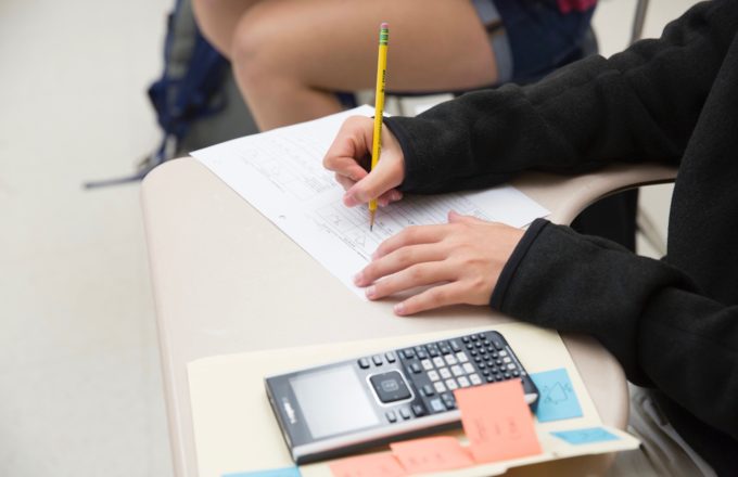 A student completing math problems on a desk with a calculator