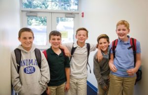 A group of 5 young male students standing by the window