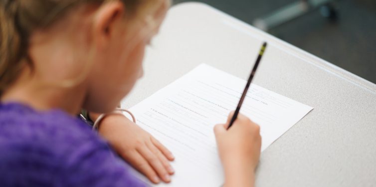 Student working at desk with paper and pencil.