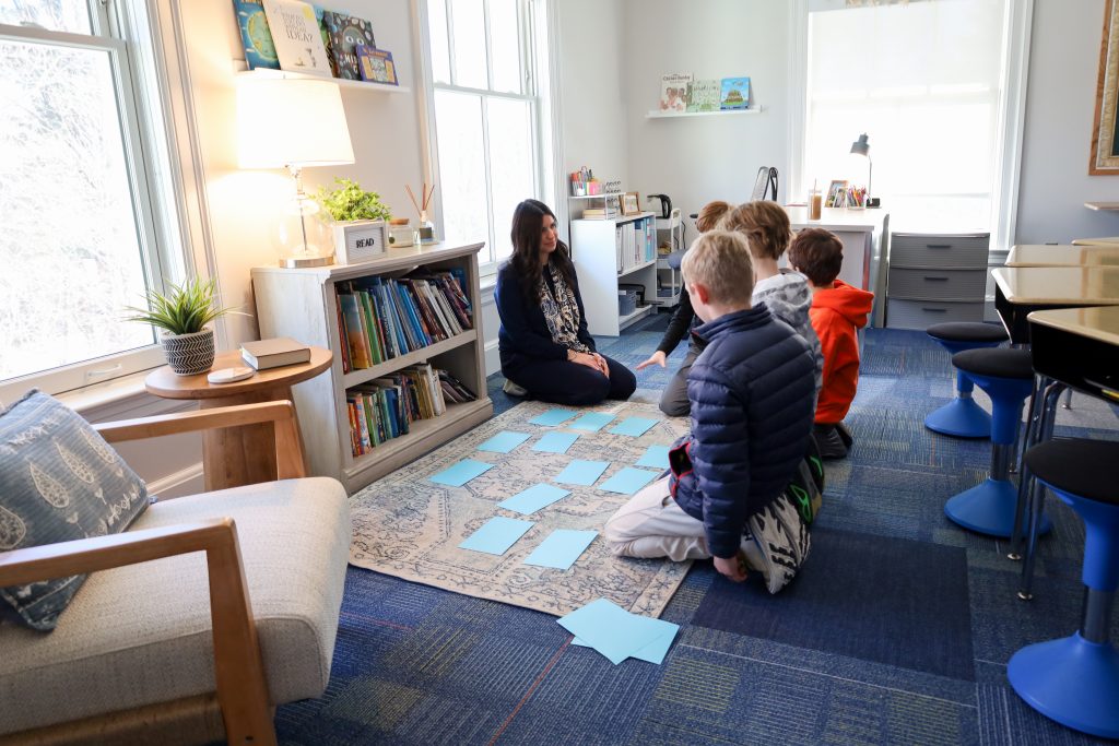 Teacher and students engaging in multisensory activity on carpet in classroom.
