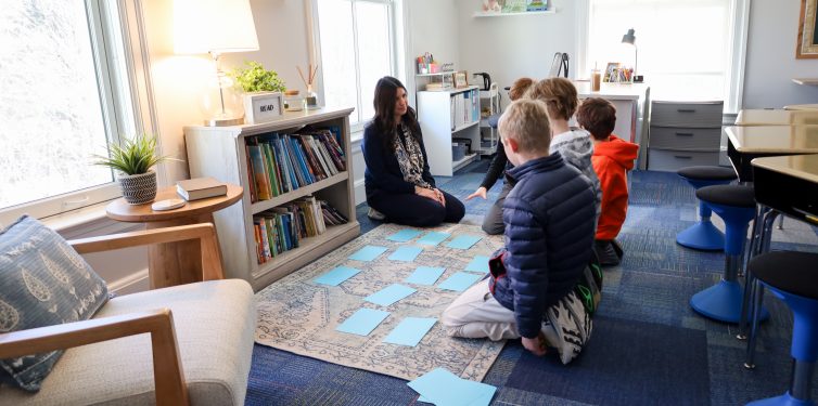 Teacher and students engaging in multisensory activity on carpet in classroom.