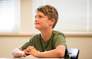A young boy sitting in a classroom looking up.