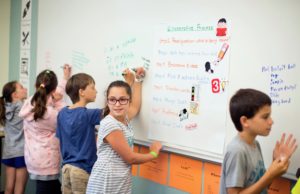 A young girl writes at a white board