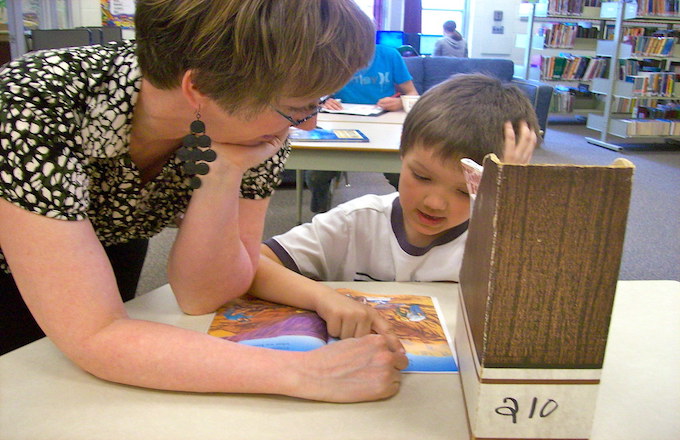 An educator measures a student's reading progress while he reads aloud
