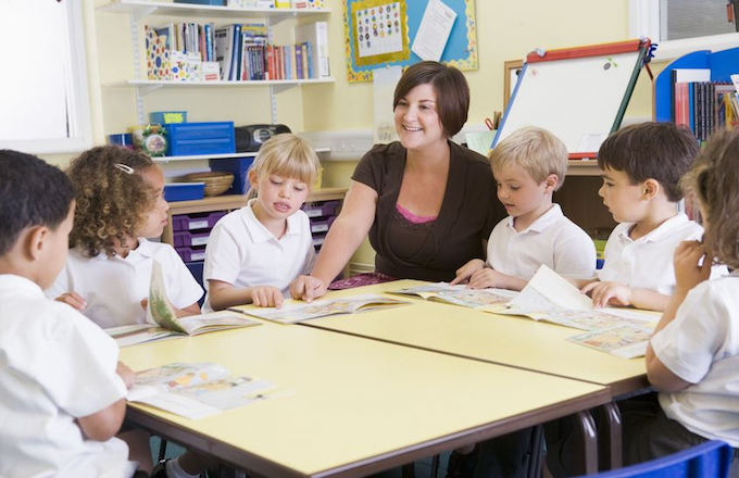 An educator models fluent oral reading while a small group of students follows along
