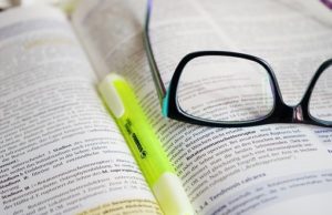Glasses resting on an open book with a highlighter in the crease of the book