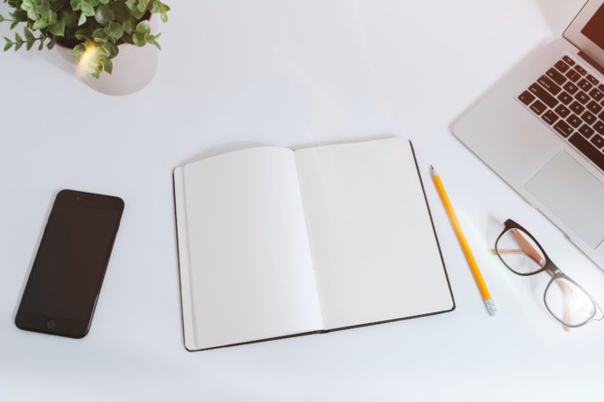 An open blank notebook sitting on a clean white desk.
