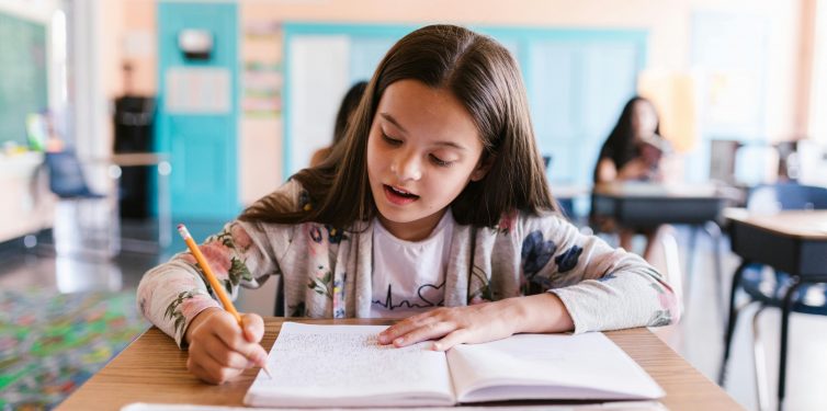 Young student sitting at desk with open notebook and pencil working on a writing assignment.