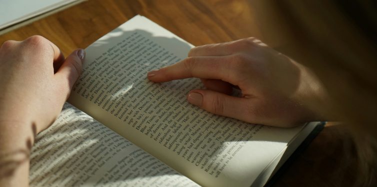 Student reading an open book using finger to track progress.