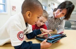 Children reading on an ipad with a teacher assisting them